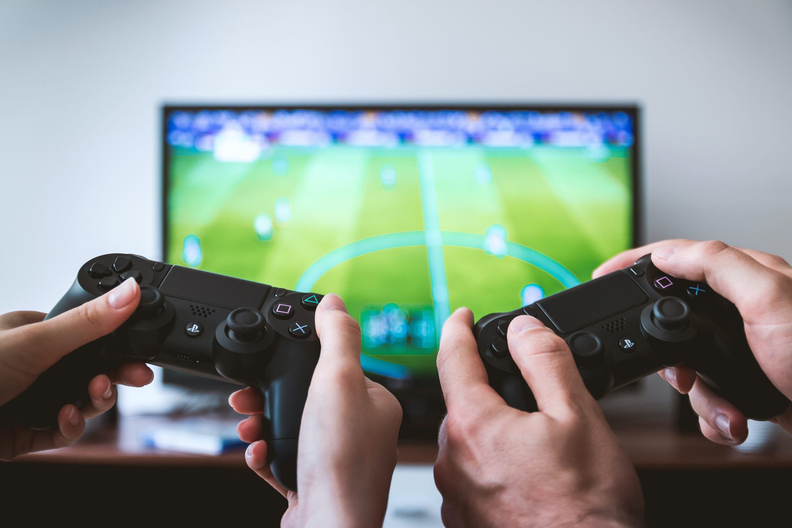 Two controllers being held in front of a TV playing FIFA