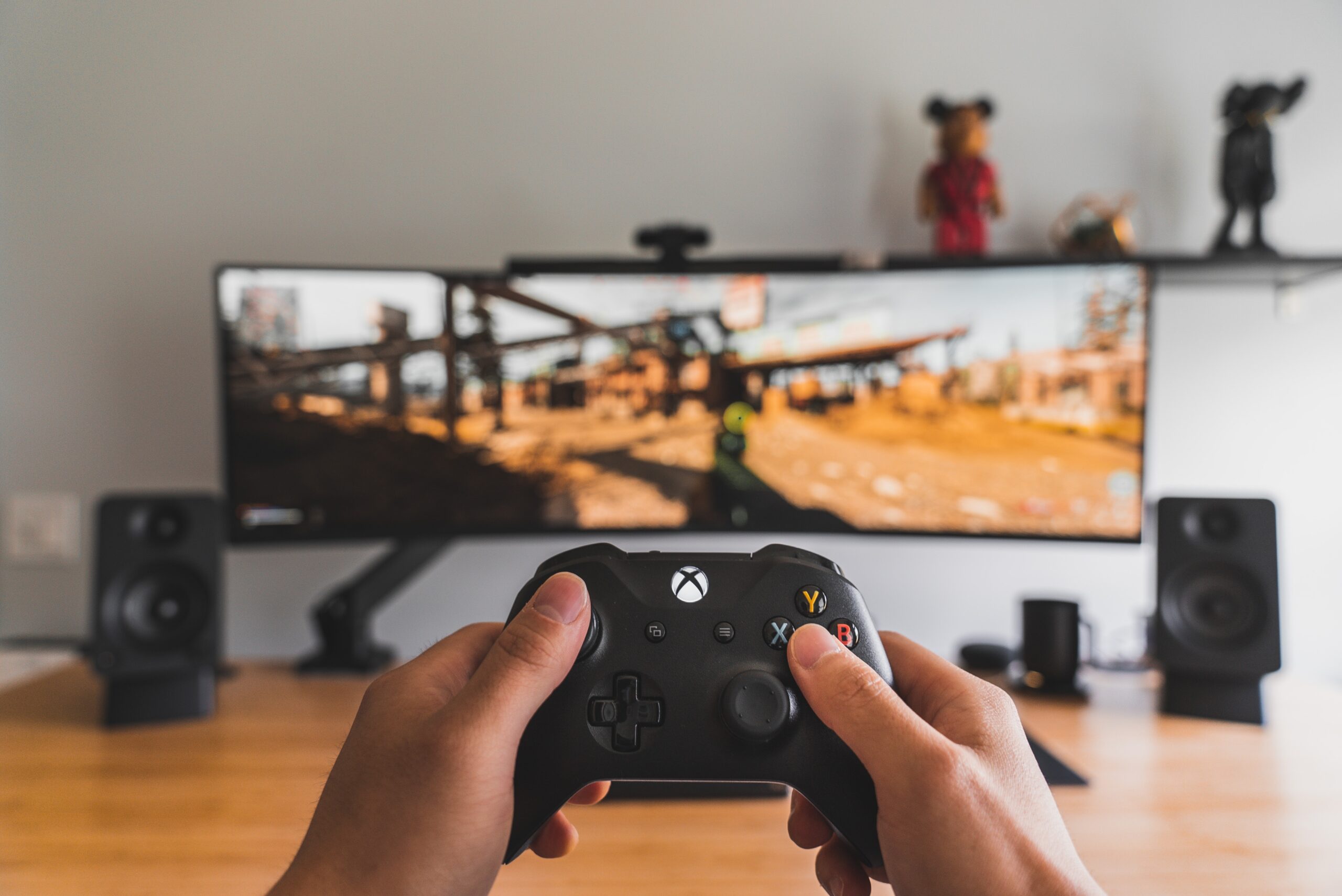 Two hands hold an Xbox controller in front of a a wide display